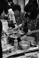 A member of Snail Union is cooking a side-dish with the help of a lady janitor from Yonsei University, a one-day cooking teacher.